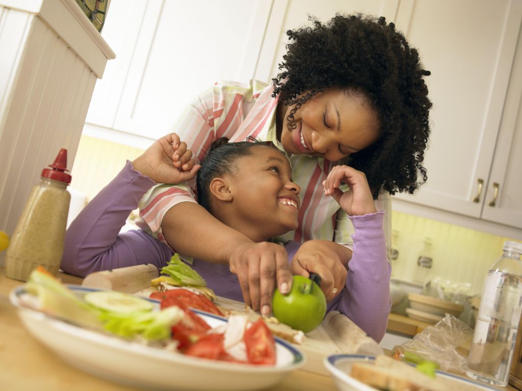 Mother Stands With Her Young Daughter in the Kitchen, Chopping an Apple for Her Lunch