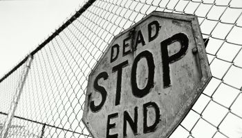 'Stop, Dead End' sign on chain link fence (B&W)