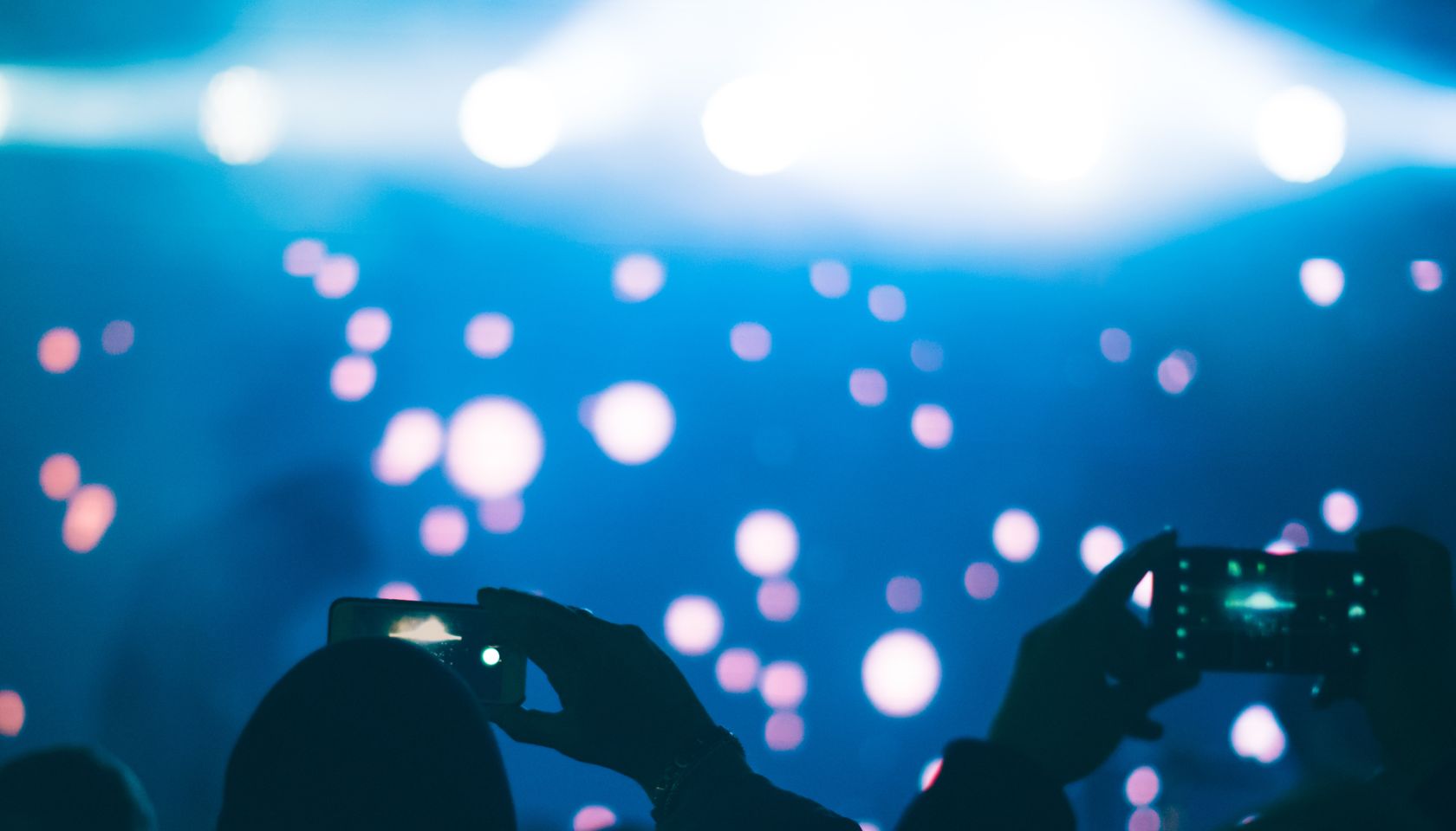 Audience members taking photos with mobile phones in a concert, against stage & spotlights