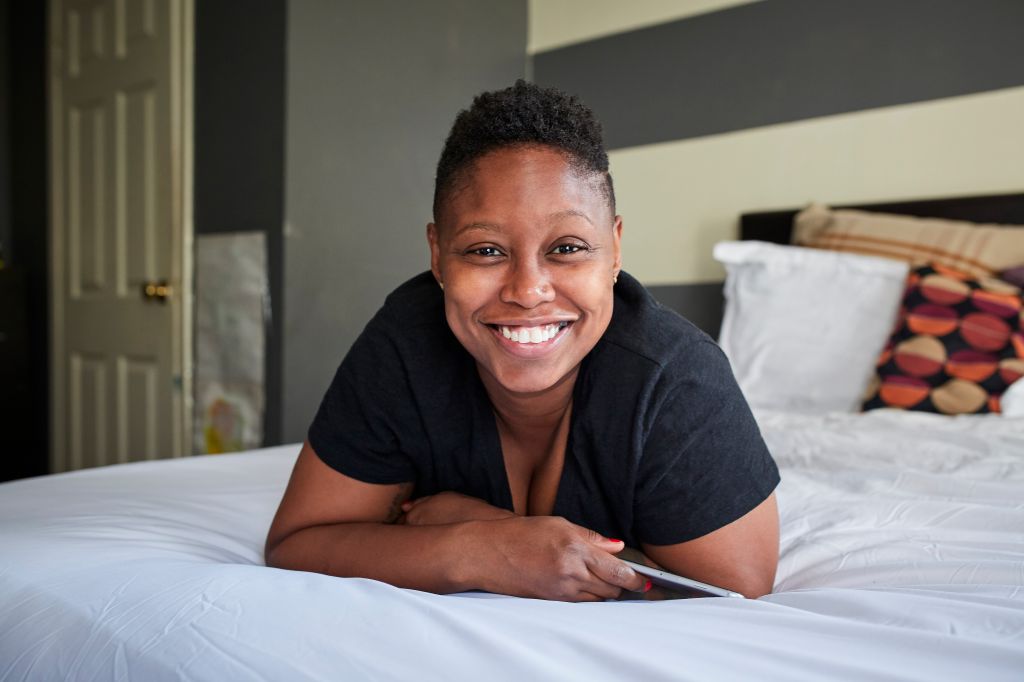 Smiling Black woman laying on bed holding cell phone