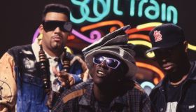 Hip Hop group Public Enemy stand in front of the neon Soul Train sign.