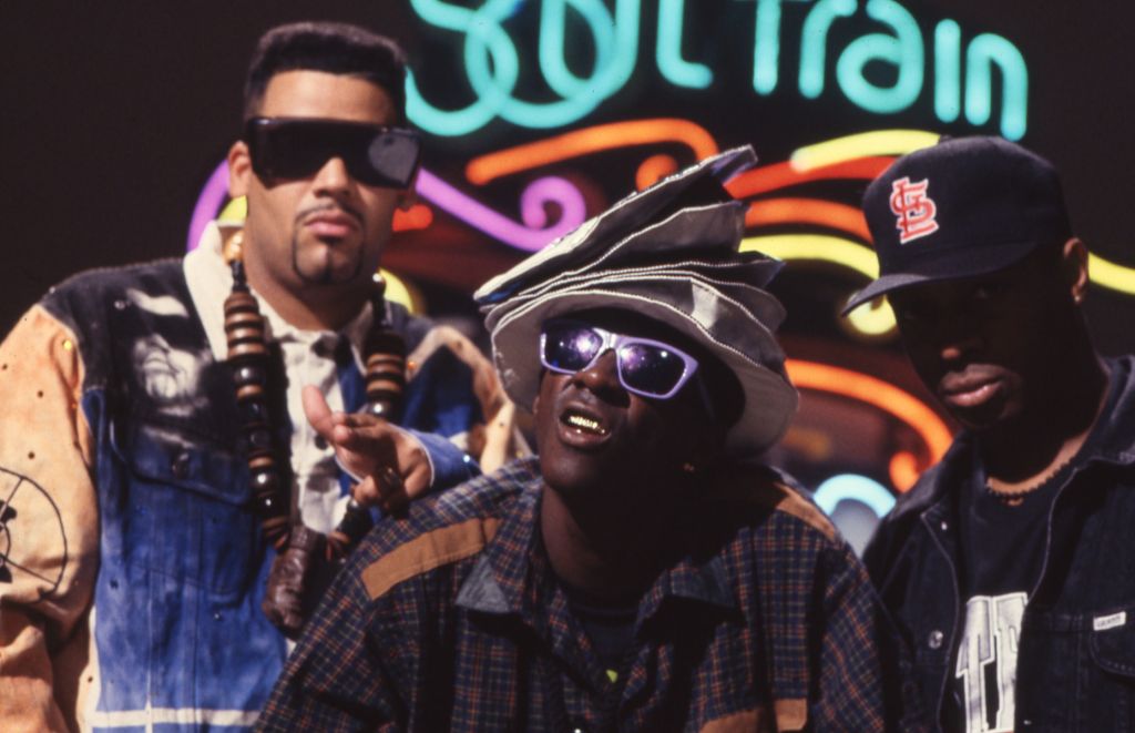 Hip Hop group Public Enemy stand in front of the neon Soul Train sign.