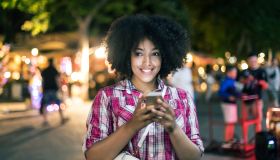 Smiling woman using smart phone on street at night