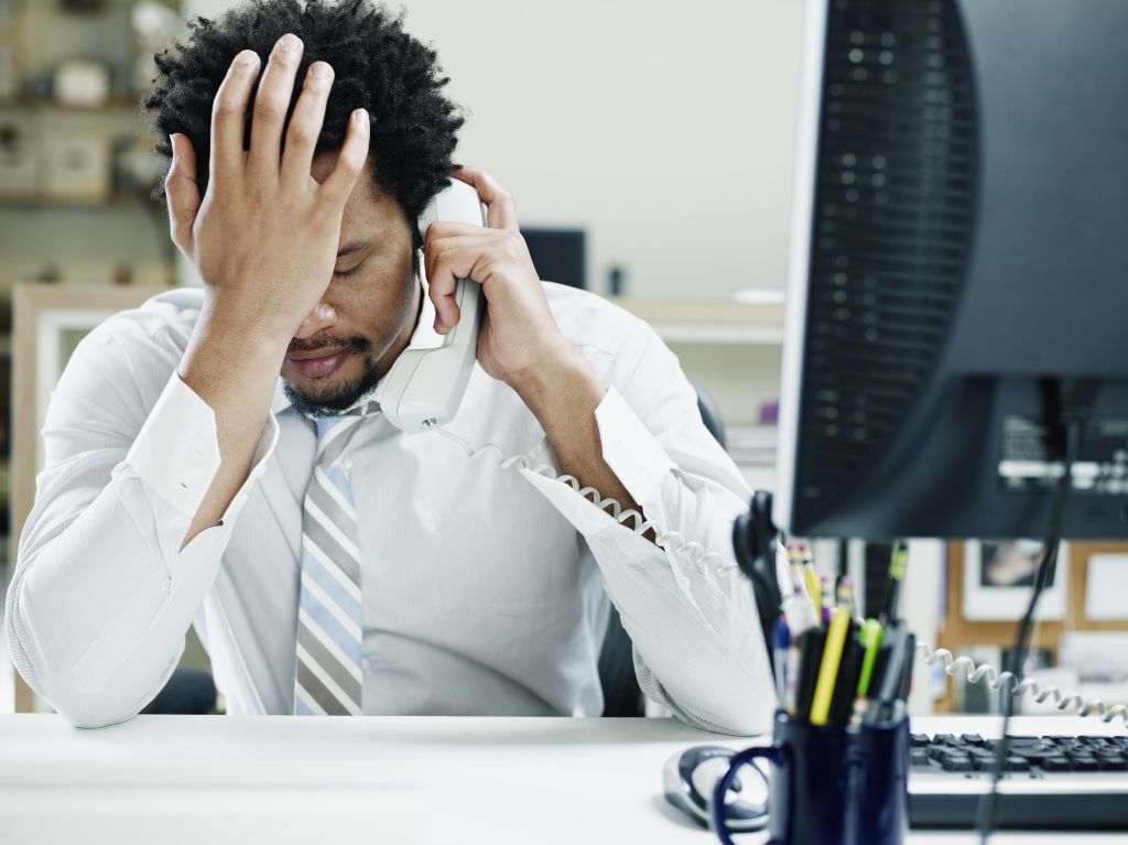 Businessman on phone at desk hand on forehead