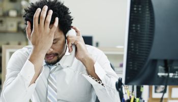 Businessman on phone at desk hand on forehead