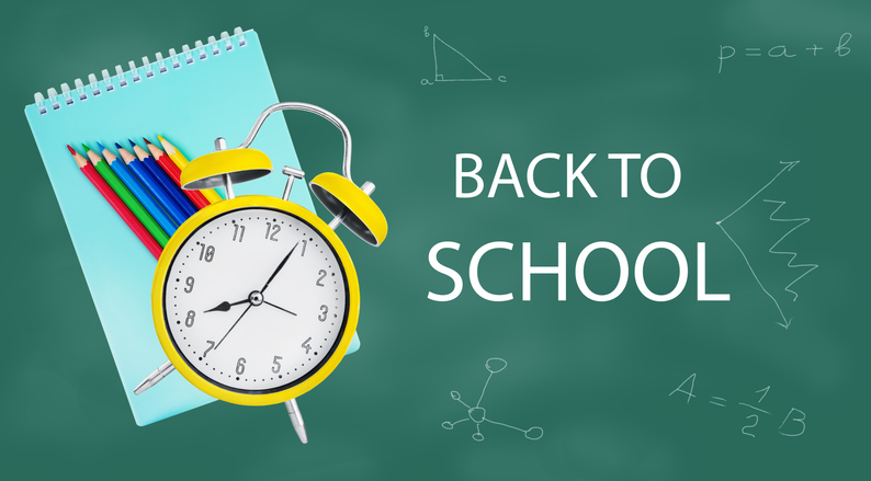 Yellow alarm clock,notebook, and colored pencils against a chalkboard with drawings. Back to school. Learning concept.